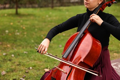 Photo of Young woman playing cello outdoors, closeup view