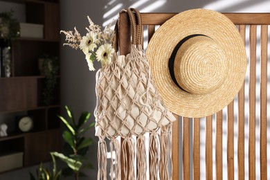 Photo of Handmade macrame shopping bag with flowers and straw hat on wooden chair indoors, space for text