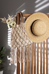 Photo of Handmade macrame shopping bag with flowers and straw hat on wooden chair indoors