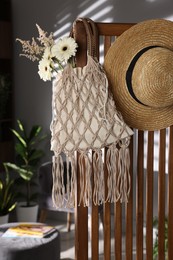 Photo of Handmade macrame shopping bag with flowers and straw hat on wooden chair indoors