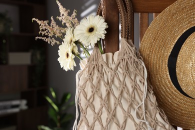 Photo of Handmade macrame shopping bag with flowers and straw hat on wooden chair indoors