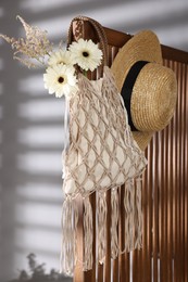 Photo of Handmade macrame shopping bag with flowers and straw hat on wooden chair indoors