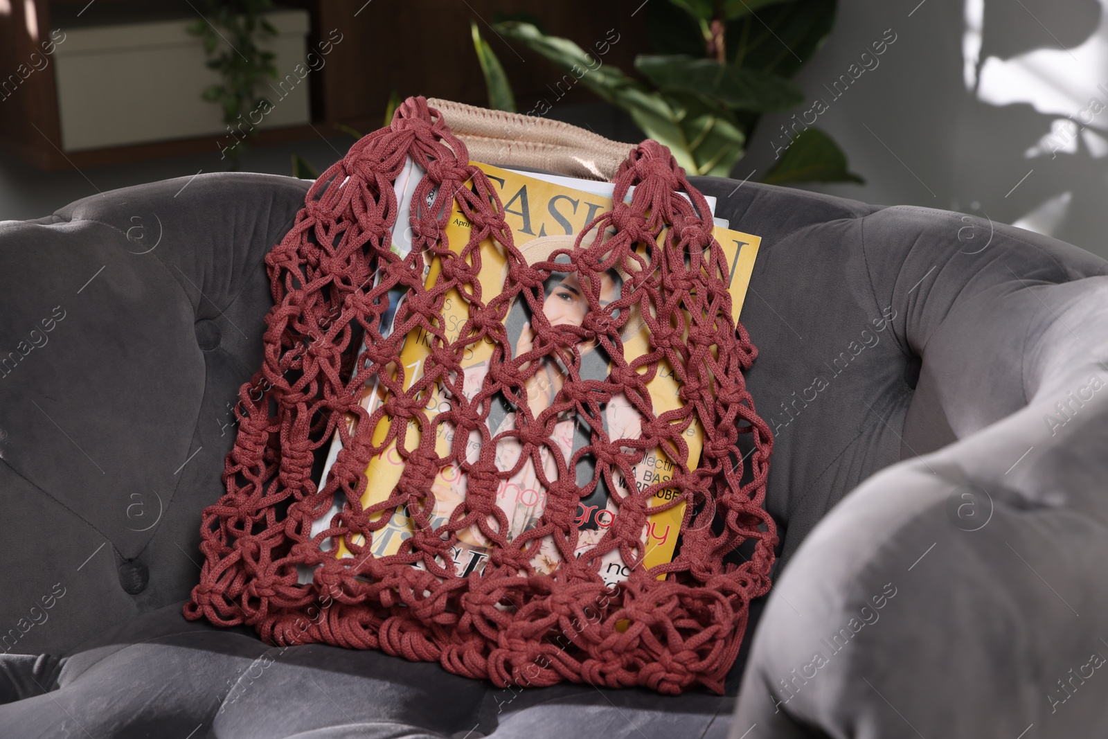 Photo of Handmade macrame shopping bag with magazines on armchair indoors