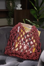 Photo of Handmade macrame shopping bag with magazines on armchair indoors