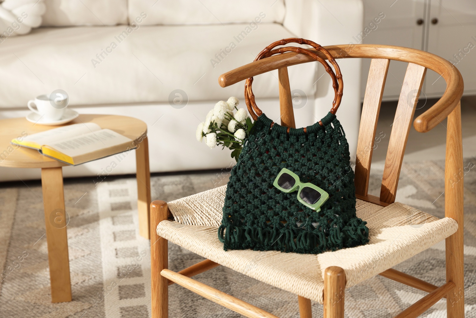 Photo of Handmade macrame shopping bag with flowers and sunglasses on chair indoors