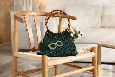 Photo of Handmade macrame shopping bag with flowers and sunglasses on chair indoors