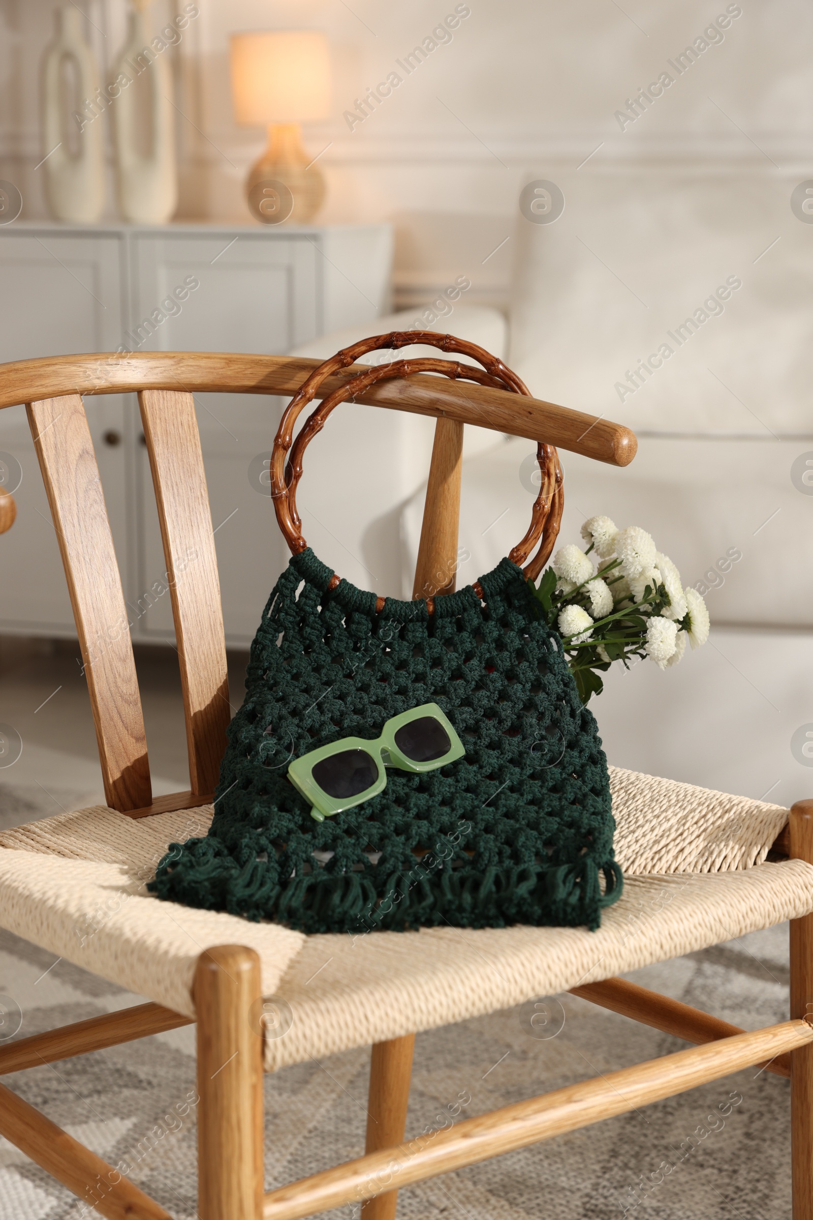 Photo of Handmade macrame shopping bag with flowers and sunglasses on chair indoors