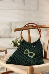 Photo of Handmade macrame shopping bag with flowers and sunglasses on chair indoors