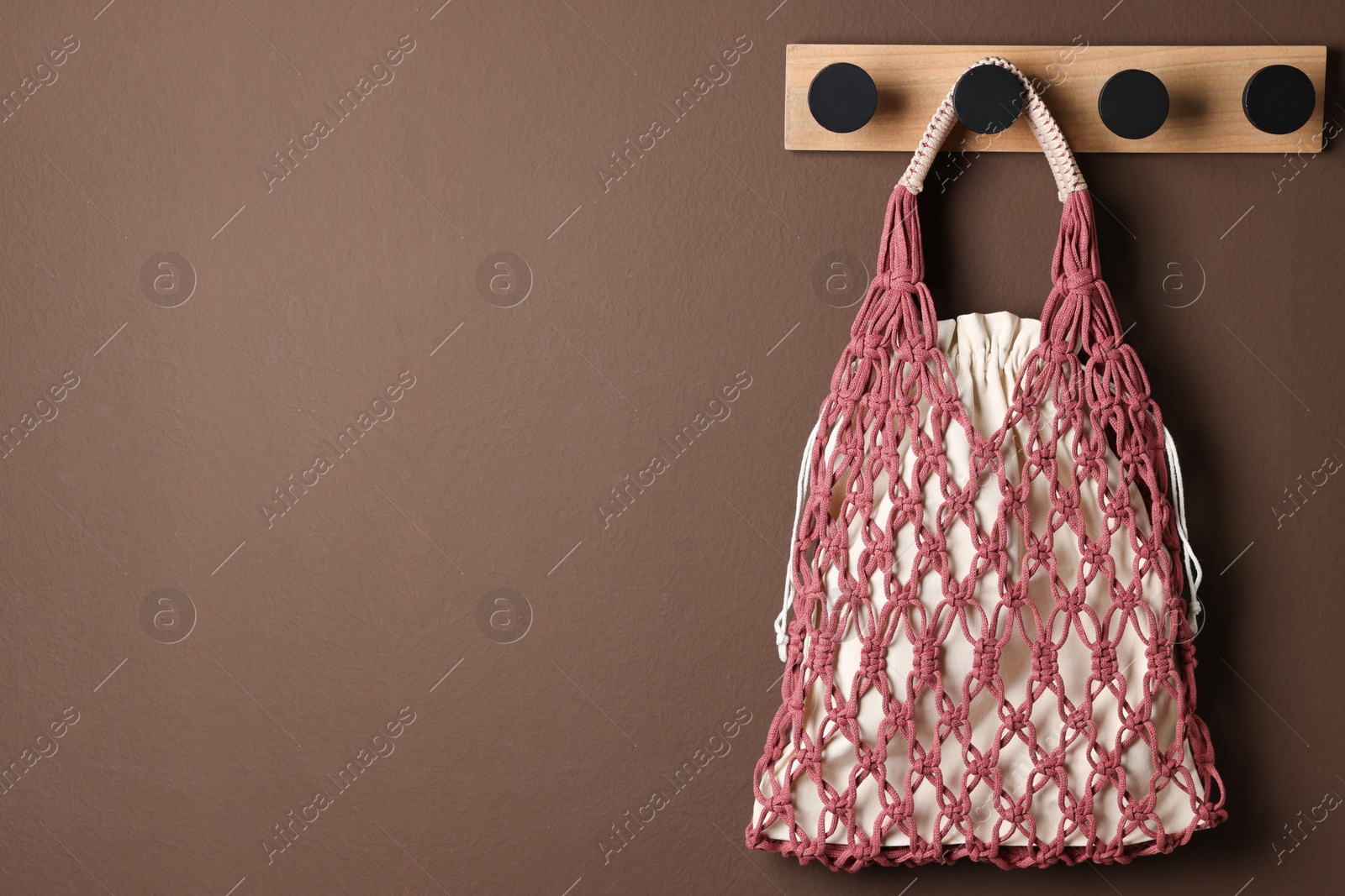 Photo of Handmade macrame shopping bag on brown wall, space for text