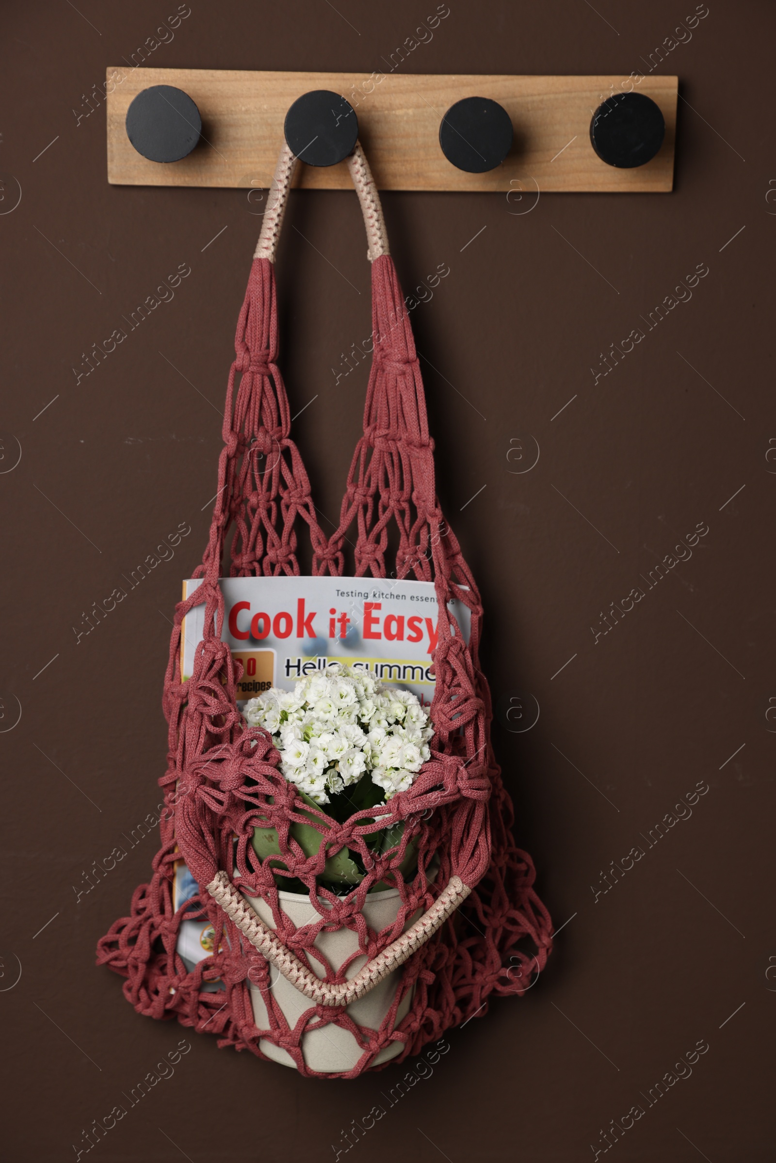 Photo of Handmade macrame shopping bag with magazine and flowers on brown wall