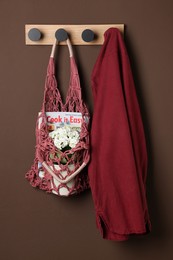 Photo of Handmade macrame shopping bag with magazine, flowers and shirt on brown wall