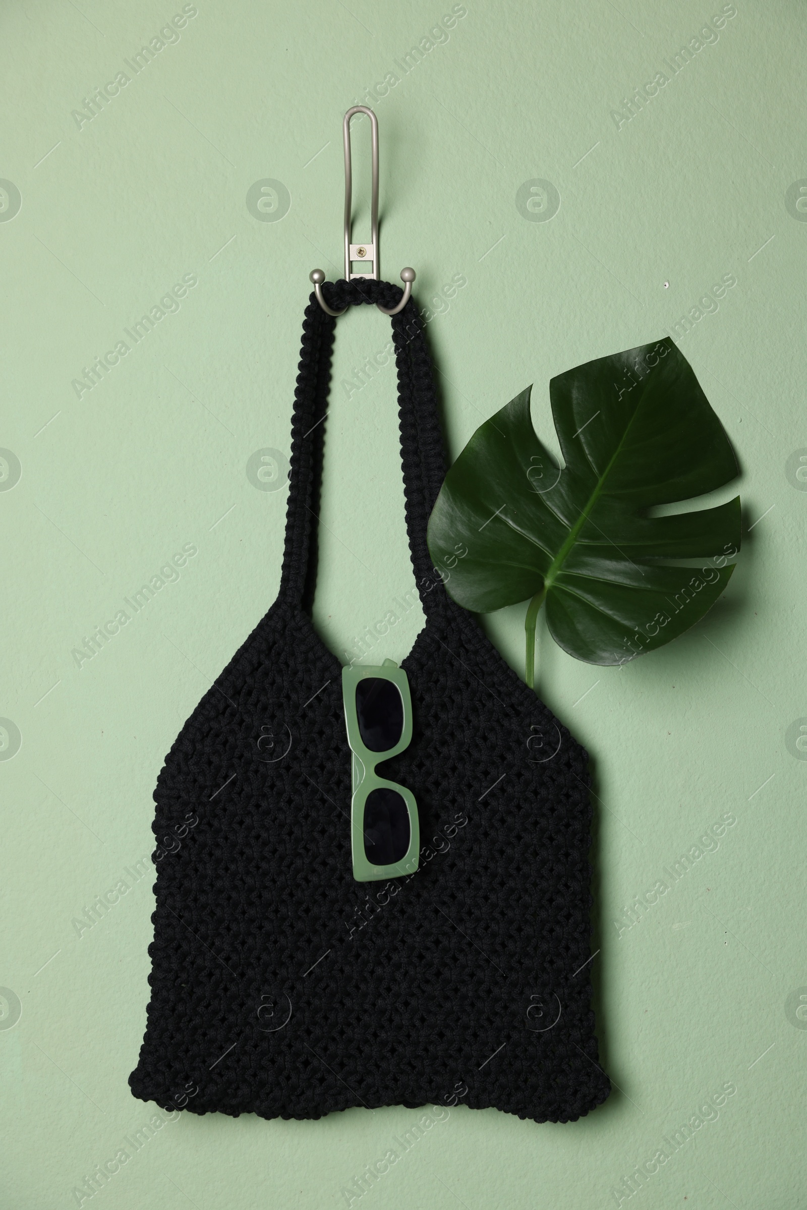 Photo of Handmade macrame shopping bag with leaf and sunglasses on light green wall