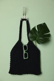 Photo of Handmade macrame shopping bag with leaf and sunglasses on light green wall