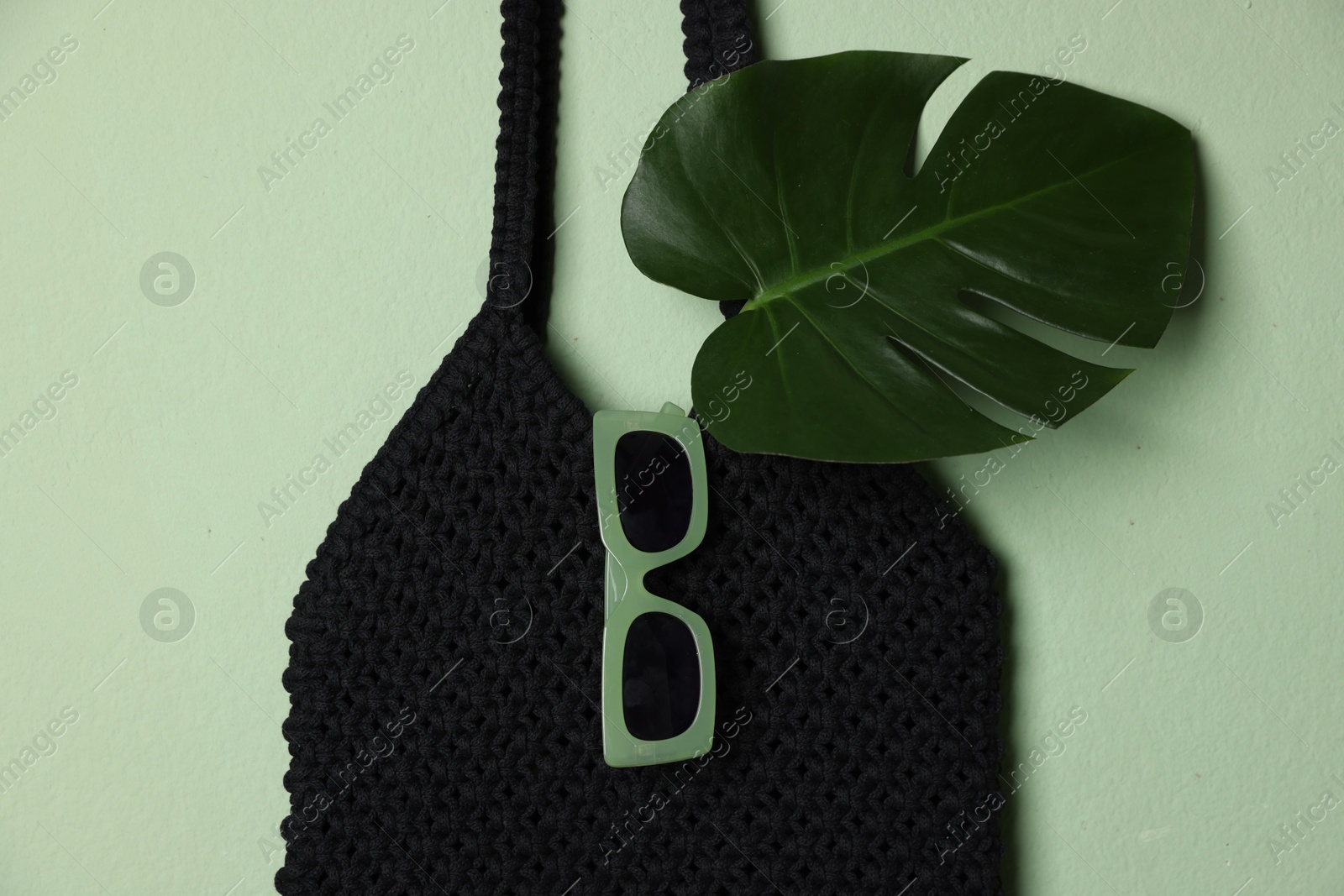 Photo of Handmade macrame shopping bag with leaf and sunglasses on light green background, top view