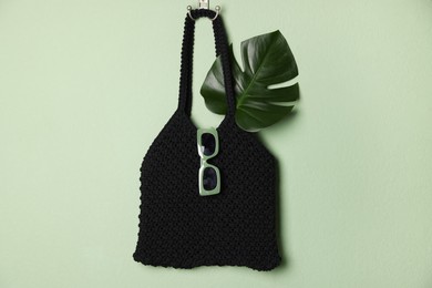 Photo of Handmade macrame shopping bag with leaf and sunglasses on light green wall