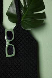 Photo of Handmade macrame shopping bag with leaf and sunglasses on light green background, top view