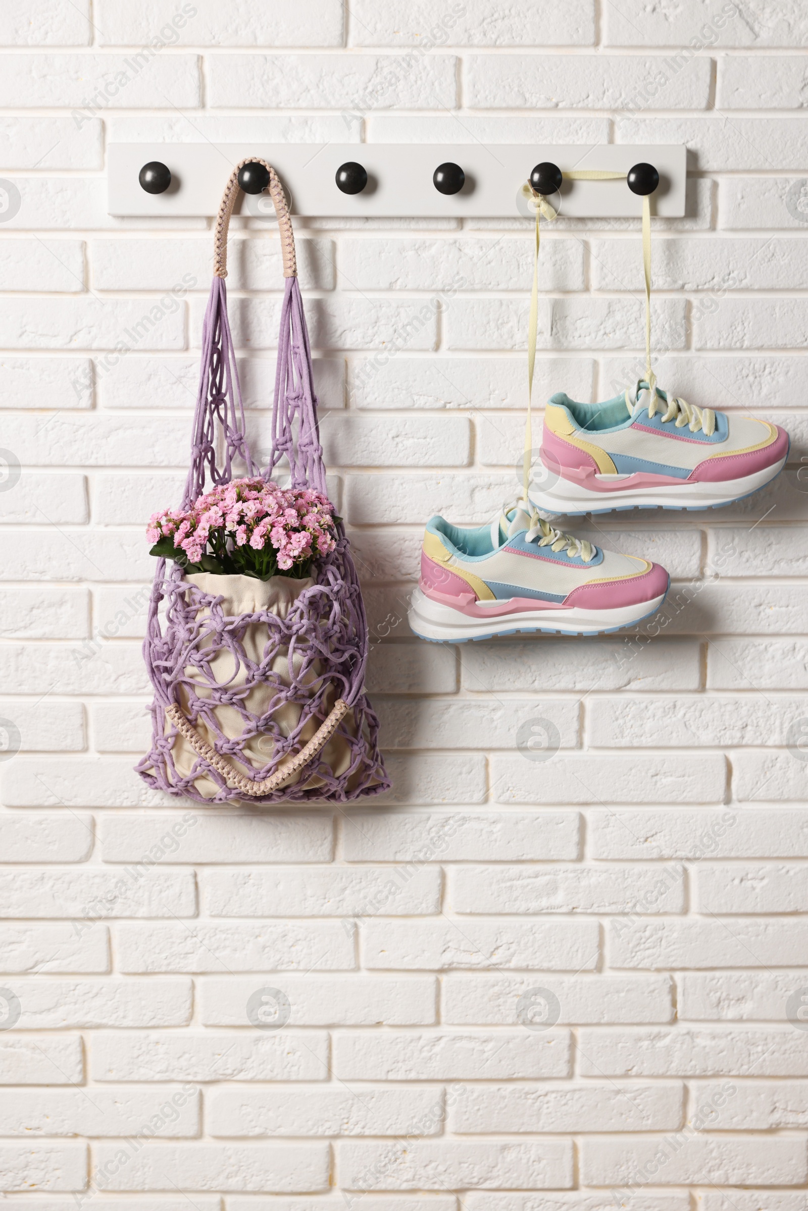 Photo of Handmade macrame shopping bag with flowers and sneakers on white brick wall