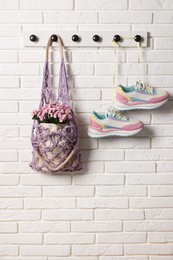 Photo of Handmade macrame shopping bag with flowers and sneakers on white brick wall