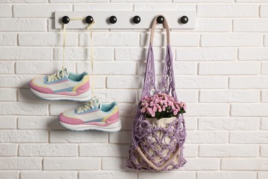 Handmade macrame shopping bag with flowers and sneakers on white brick wall