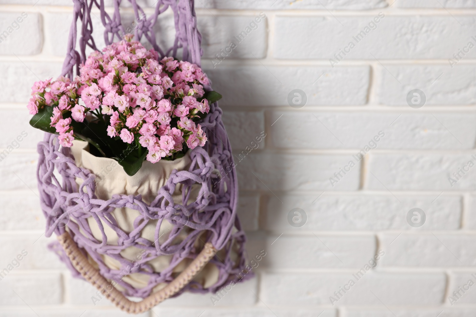 Photo of Handmade macrame shopping bag with flowers on white brick wall, space for text