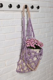 Handmade macrame shopping bag with flowers on white brick wall