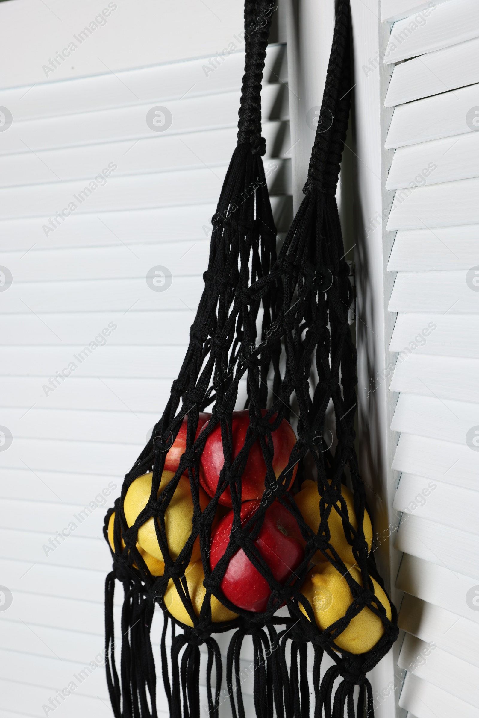 Photo of Handmade macrame shopping bag with fruits on white wall