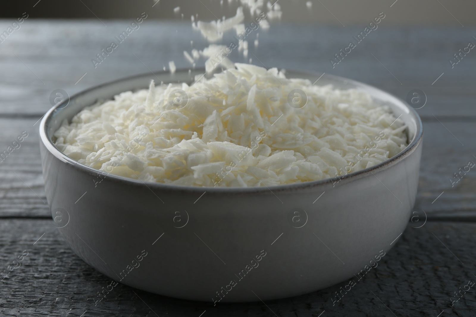 Photo of Pouring soy wax into bowl on grey wooden table, closeup