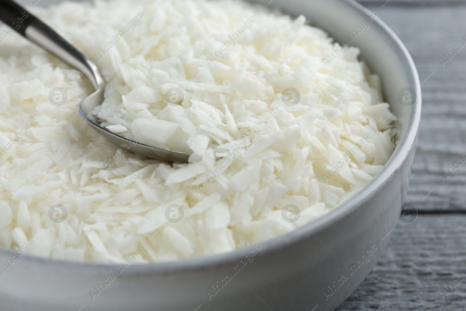 Photo of Soy wax in bowl on grey wooden table, closeup