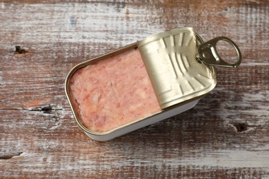 Photo of Tasty canned meat in tin can on wooden table, top view