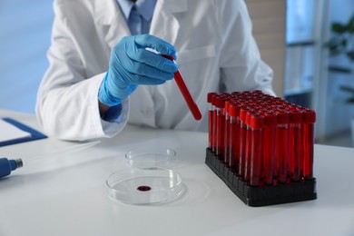 Photo of Laboratory testing. Doctor taking test tube with blood sample from rack at table indoors, closeup