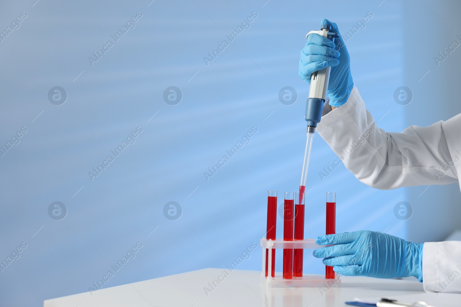 Photo of Laboratory testing. Doctor dripping blood sample into test tube at table indoors, closeup. Space for text