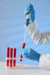 Photo of Laboratory testing. Doctor dripping blood sample into test tube at table indoors, closeup