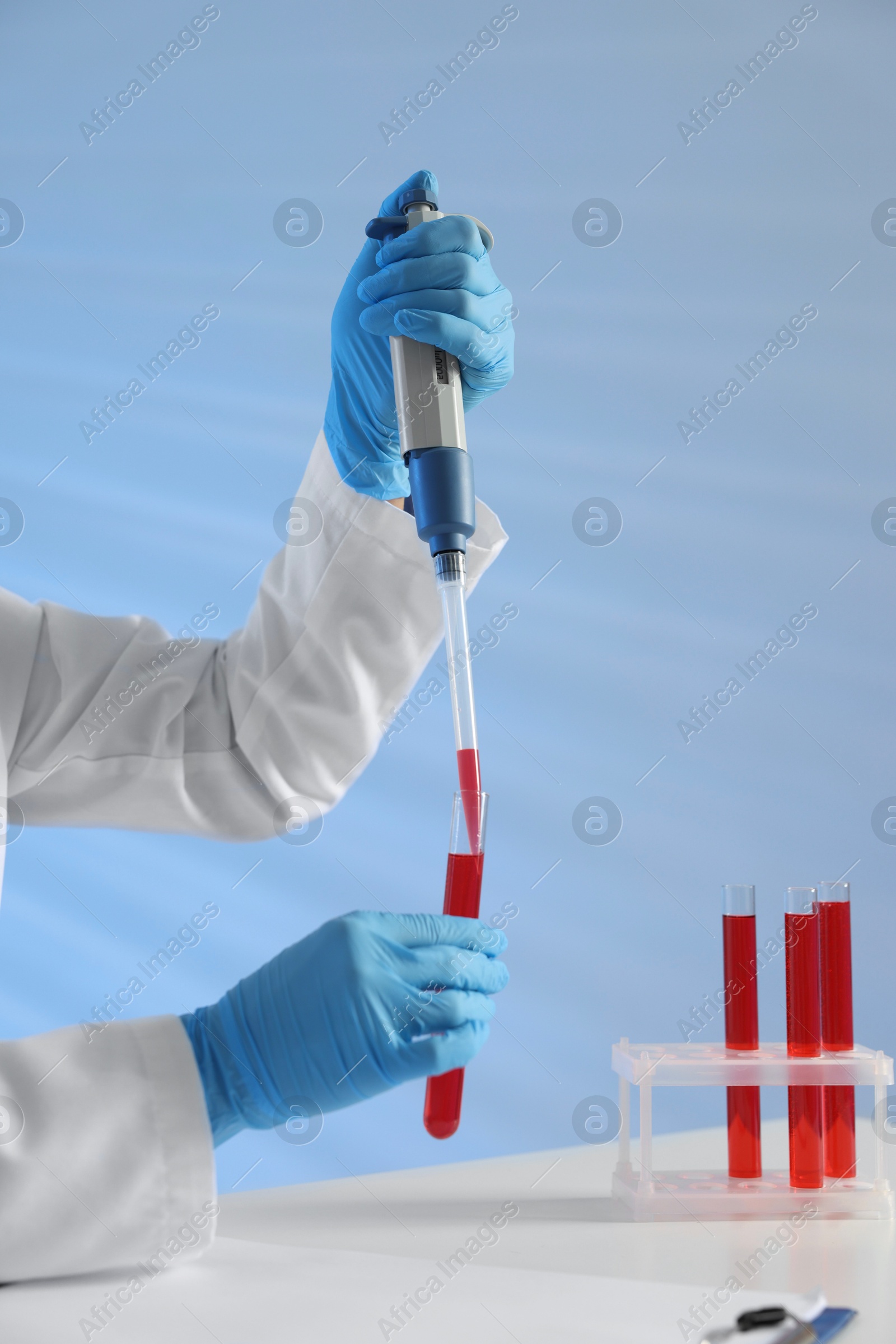 Photo of Laboratory testing. Doctor dripping blood sample into test tube at table indoors, closeup