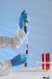 Photo of Laboratory testing. Doctor dripping blood sample into test tube at table indoors, closeup