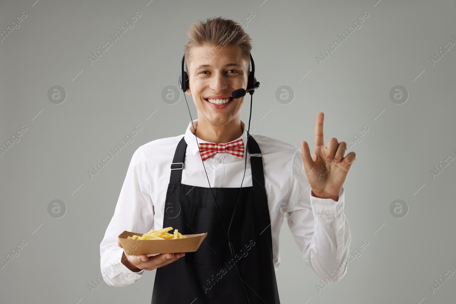 Photo of Fast-food worker holding container with French fries on gray background