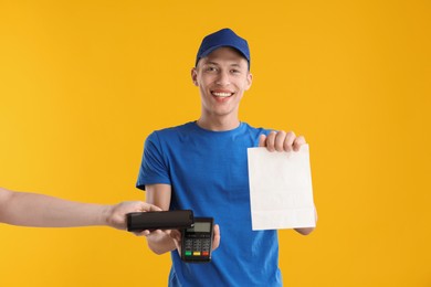 Photo of Fast-food worker taking payment from client via terminal on orange background, closeup