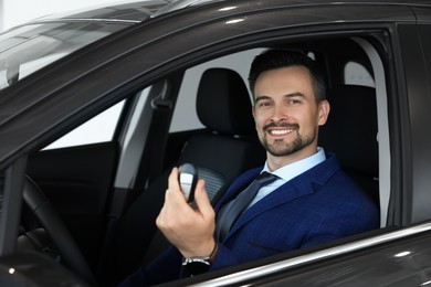 Photo of Happy salesman holding key inside new black car in salon