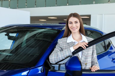 Photo of Young woman near new blue car in salon