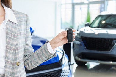 Saleswoman holding key near new car in salon, closeup