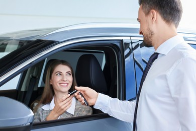 Photo of Woman giving key to man inside new car in salon