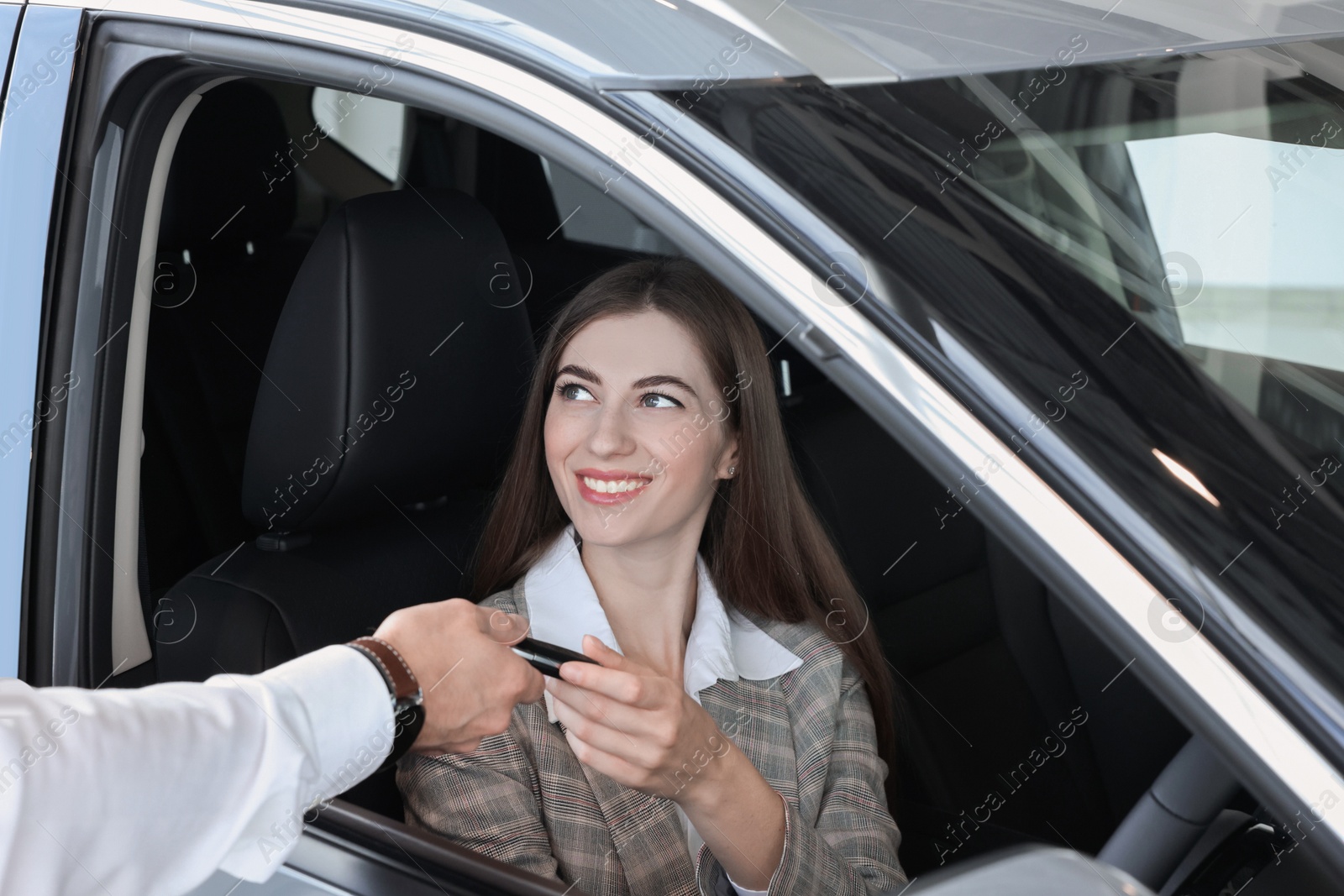 Photo of Salesman giving key to client inside new car in salon