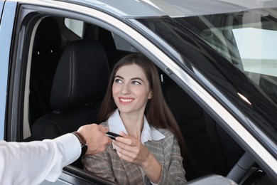 Photo of Salesman giving key to client inside new car in salon