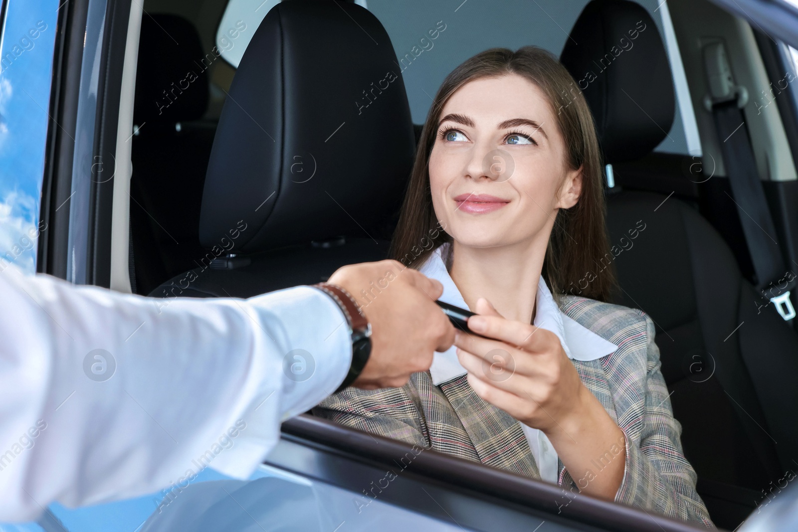 Photo of Salesman giving key to client inside new car in salon