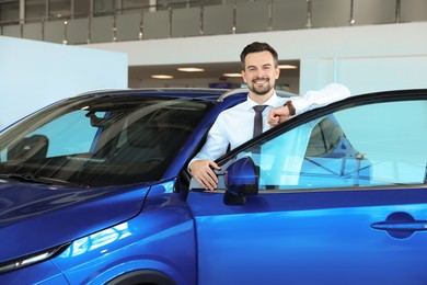 Photo of Happy man near new blue car in salon