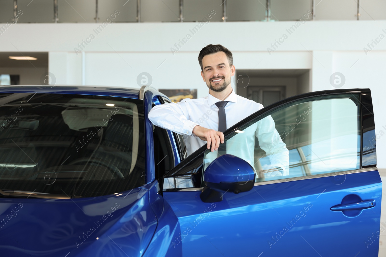 Photo of Happy man near new blue car in salon