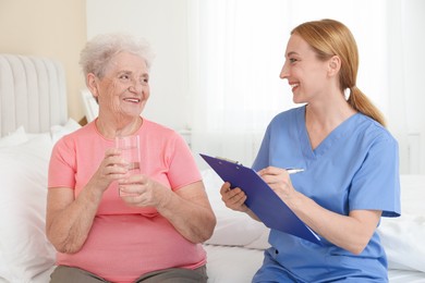 Photo of Healthcare worker with clipboard consulting senior patient on bed indoors