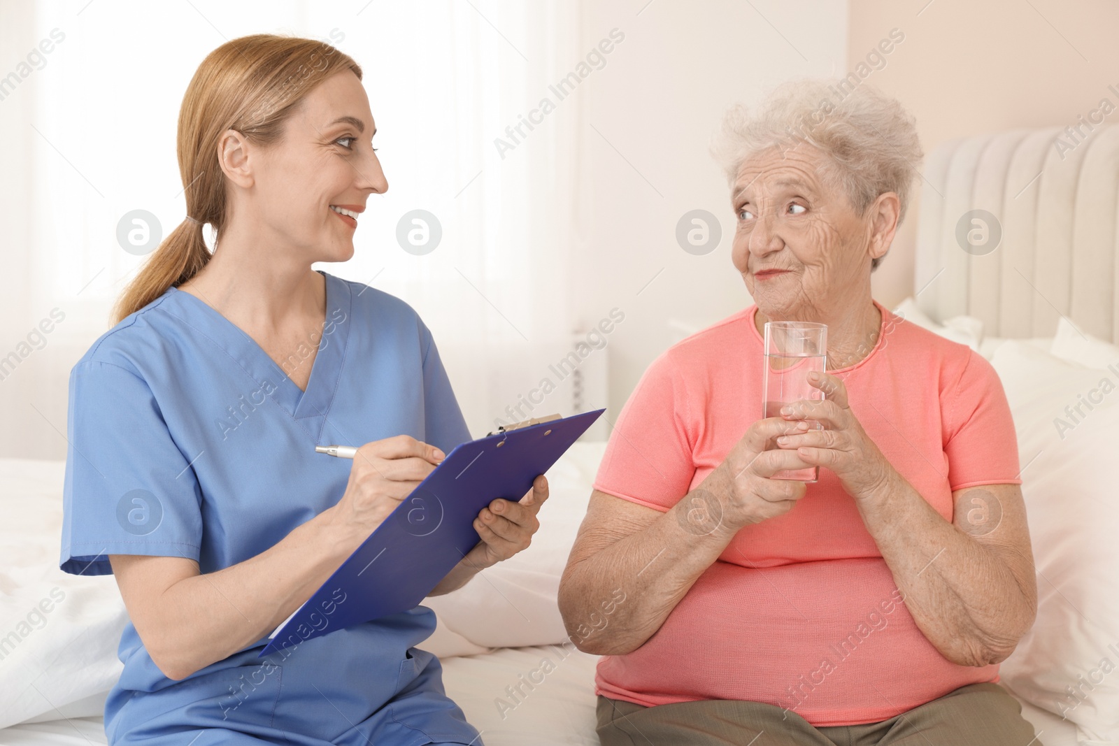 Photo of Healthcare worker with clipboard consulting senior patient on bed indoors