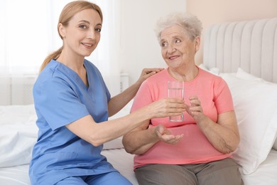 Photo of Healthcare worker giving glass of water to senior patient at home