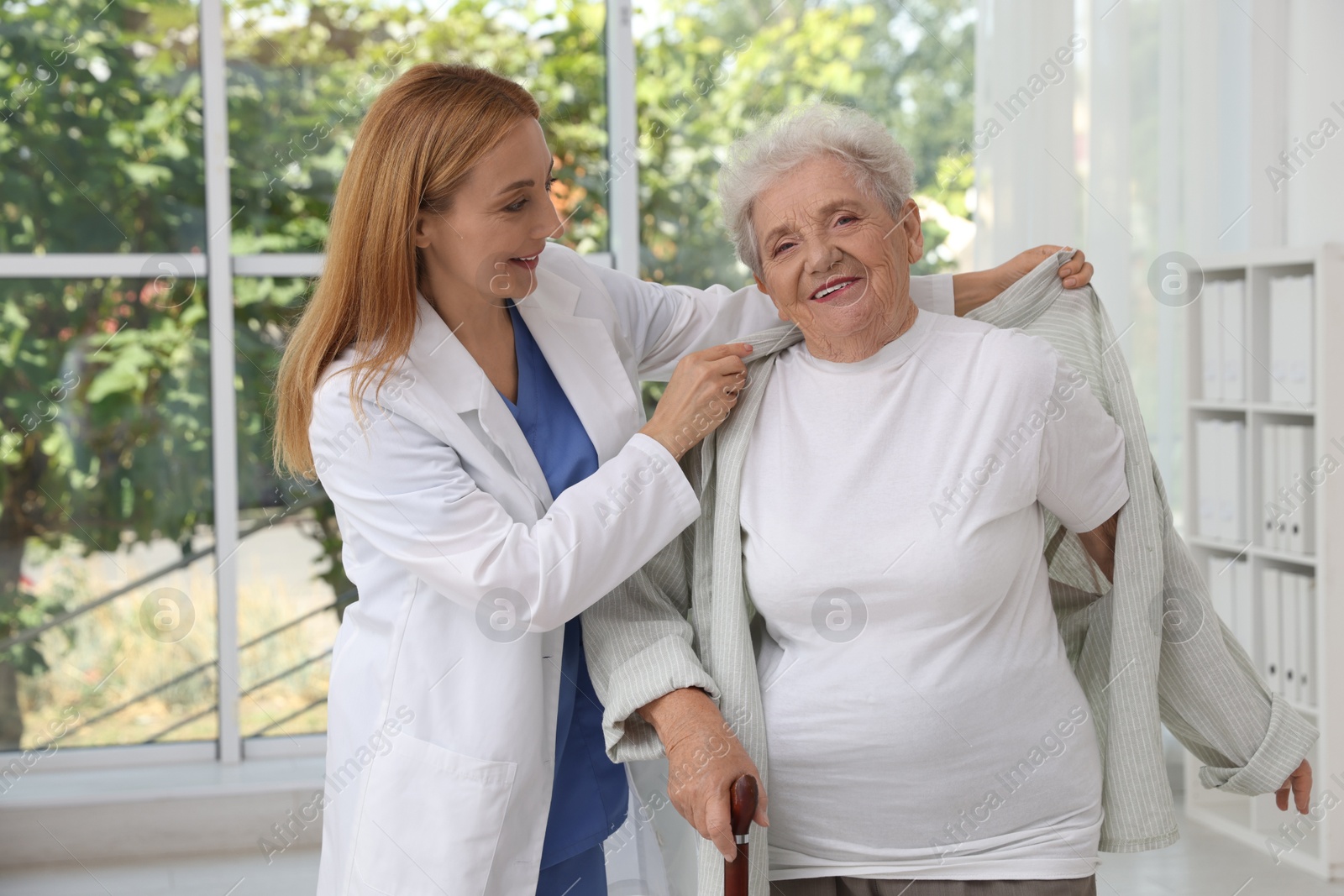 Photo of Healthcare worker helping senior patient to wear jacket in hospital