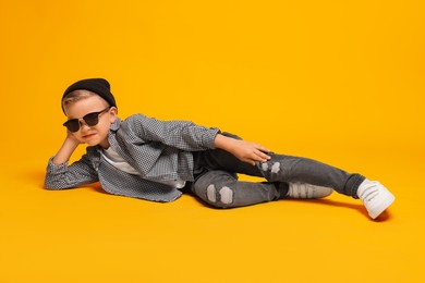 Photo of Little boy with stylish clothes and sunglasses on orange background